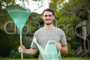 Portrait of young man standing with a gardening rake and waterin