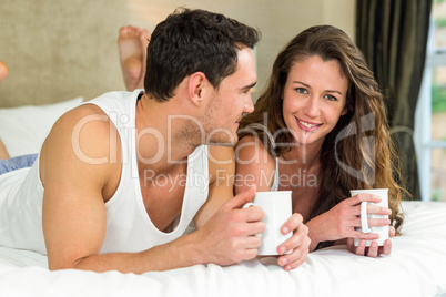 Young couple having cup of coffee on bed