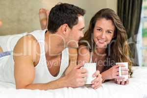 Young couple having cup of coffee on bed