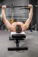 Shirtless man lifting heavy barbell on bench