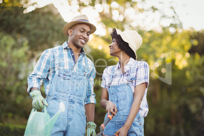 Smiling couple holding watering can and gardening shears
