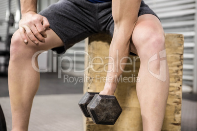 Muscular man lifting dumbbell on wooden block