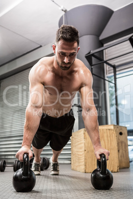 Shirtless man doing push up with kettlebells