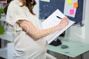 Pregnant businesswoman writing in folder