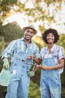 Smiling couple holding watering can and gardening shears