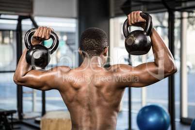 Shirtless man lifting heavy kettlebells