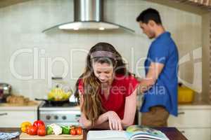 Woman checking the recipe book and man cooking on stove