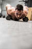 Shirtless man doing push up with dumbbells