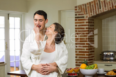 Man embracing while woman feeding strawberry to him