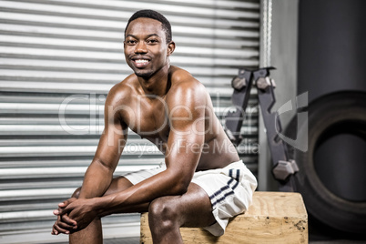 Smiling shirtless man sitting on wooden block