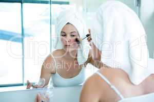 woman applying face powder in the bathroom mirror