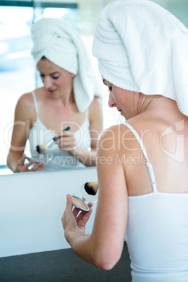 woman applying face powder in the bathroom mirror