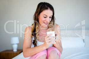 brunette woman peering into a cup while sitting on her bed