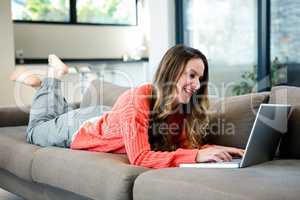 smiling woman lying on the couch on her laptop
