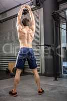 Rear view of shirtless man lifting heavy kettlebell