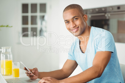 Smiling man using laptop and smartphone