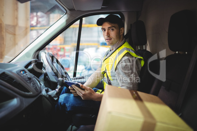Delivery driver using tablet in van with parcels on seat