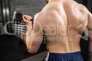 Rear view of shirtless man lifting heavy dumbbells