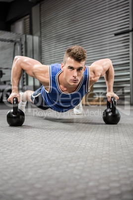 Muscular man doing push up with kettlebells