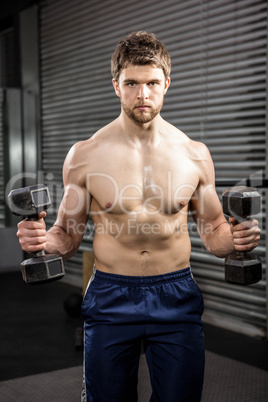 Shirtless man lifting heavy dumbbells