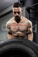 Shirtless man flipping heavy tire