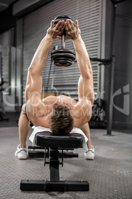 Shirtless man lifting heavy dumbbell on bench