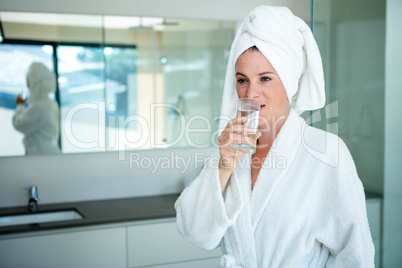 woman in a dressing gown drinking a glass of water