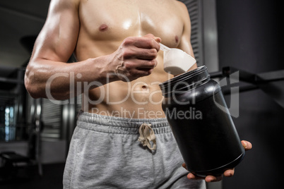 Mid section of shirtless man taking proteins from can