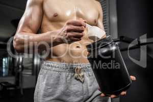 Mid section of shirtless man taking proteins from can