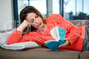thoughtful woman lying on the couch reading a book