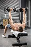 Shirtless man lifting heavy dumbbells on bench