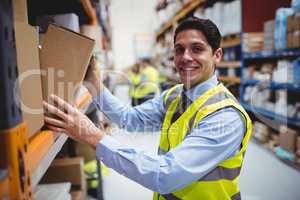 Smiling warehouse worker taking package in the shelf