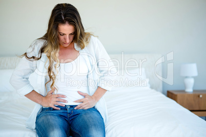 woman sitting on her bed holding her stomach