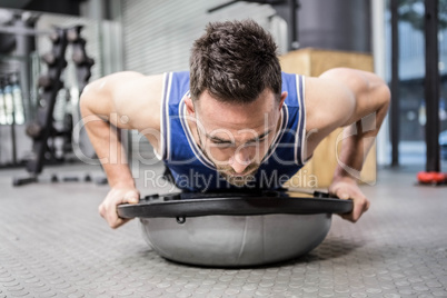 Muscular man doing push up on bosu ball