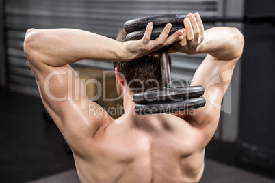 Rear view of shirtless man lifting heavy dumbbell