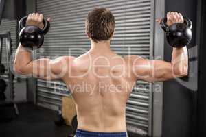 Rear view of shirtless man lifting heavy kettlebells