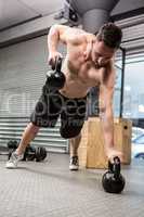 Shirtless man doing push up with kettlebells