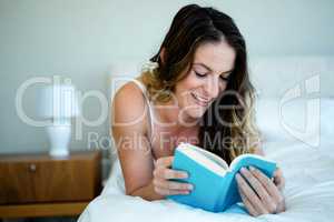 smiling woman reading a book in bed