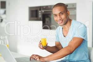 Smiling man using laptop and drinking orange juice