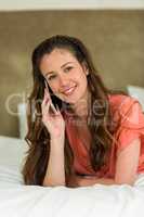 Young woman in bed talking on mobile phone