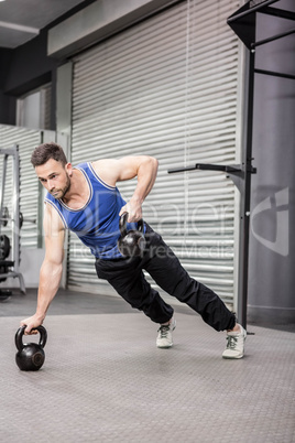 Muscular man doing push up with kettlebells