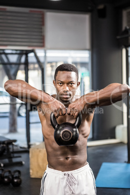 Shirtless man lifting heavy kettlebell