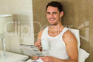 Young man reading newspaper while holding a cup of tea