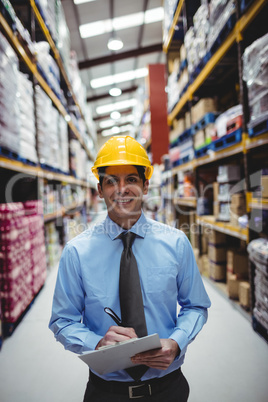 Smiling warehouse manager writing on clipboard