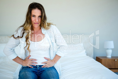 woman sitting on her bed gripping her  stomach