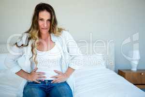 woman sitting on her bed gripping her  stomach