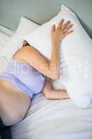 Pregnant woman covering face with pillow