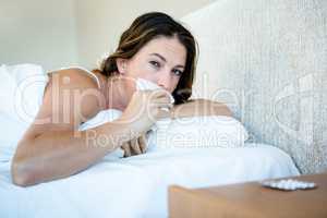 Sick woman in bed wiping her nose