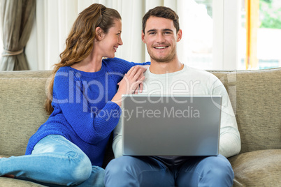 Young couple smiling face to face on sofa and using laptop