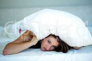 woman hiding in bed covering herself with a pillow